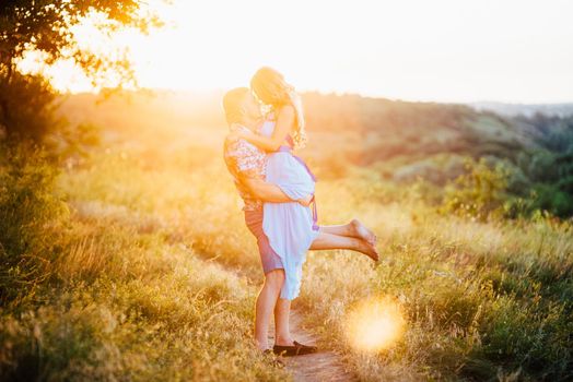 blonde girl with loose hair in a light blue dress and a guy in the light of sunset in nature