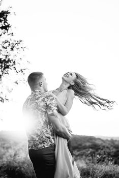 blonde girl with loose hair in a light blue dress and a guy in the light of sunset in nature