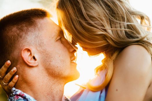 blonde girl with loose hair in a light blue dress and a guy in the light of sunset in nature