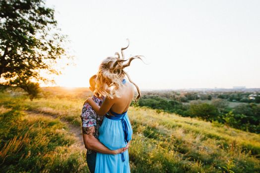 blonde girl with loose hair in a light blue dress and a guy in the light of sunset in nature