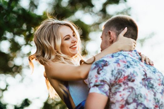 blonde girl with loose hair in a light blue dress and a guy in the light of sunset in nature