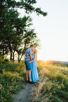 blonde girl with loose hair in a light blue dress and a guy in the light of sunset in nature