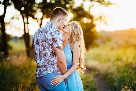 blonde girl with loose hair in a light blue dress and a guy in the light of sunset in nature