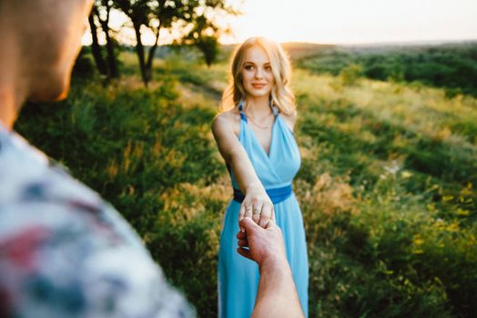 blonde girl with loose hair in a light blue dress and a guy in the light of sunset in nature