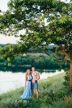 blonde girl with loose hair in a light blue dress and a guy in the light of sunset in nature