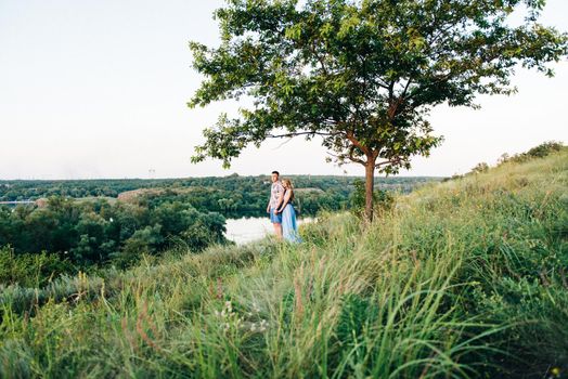 blonde girl with loose hair in a light blue dress and a guy in the light of sunset in nature