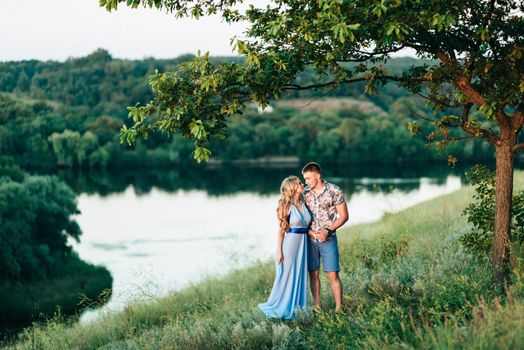 blonde girl with loose hair in a light blue dress and a guy in the light of sunset in nature