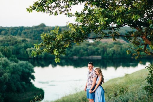 blonde girl with loose hair in a light blue dress and a guy in the light of sunset in nature