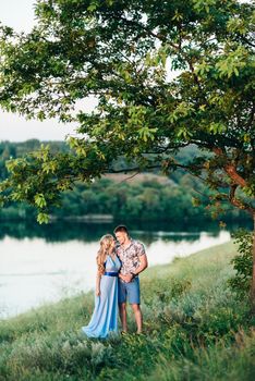 blonde girl with loose hair in a light blue dress and a guy in the light of sunset in nature