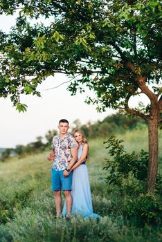 blonde girl with loose hair in a light blue dress and a guy in the light of sunset in nature