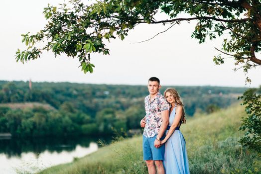 blonde girl with loose hair in a light blue dress and a guy in the light of sunset in nature