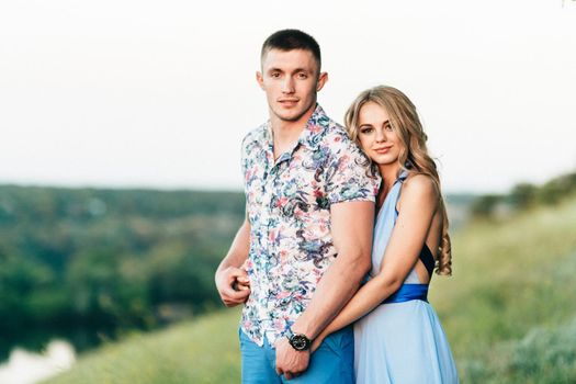 blonde girl with loose hair in a light blue dress and a guy in the light of sunset in nature