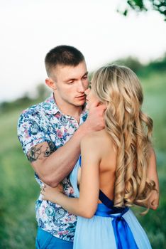 blonde girl with loose hair in a light blue dress and a guy in the light of sunset in nature