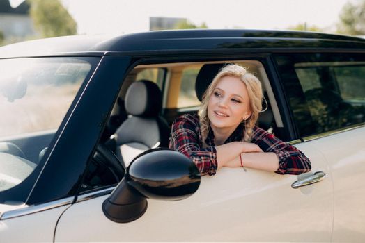 blonde with pigtails in a shirt, jeans, red shoes and black glasses near a white car