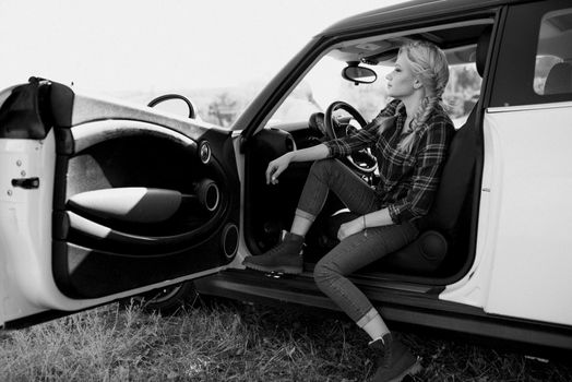 blonde with pigtails in a shirt, jeans, red shoes and black glasses near a white car