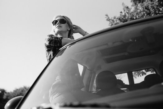 blonde with pigtails in a shirt, jeans, red shoes and black glasses near a white car