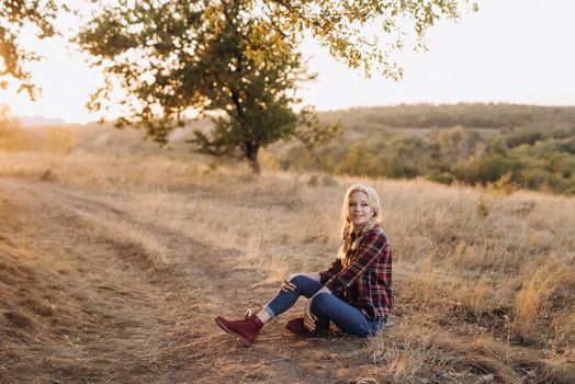 blonde with pigtails in a shirt, jeans, red shoes smiling at sunset