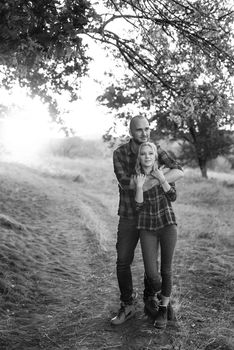 Cheerful guy with a board and a blonde girl for a walk in plaid shirts at sunset