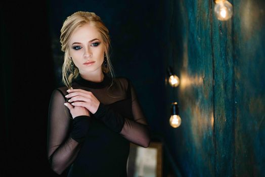 Blonde girl with blue eyes in a black dress in a dark turquoise interior