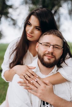 young couple in love a guy with a beard and a girl with dark hair in light clothes in the green forest