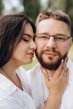 young couple in love a guy with a beard and a girl with dark hair in light clothes in the green forest