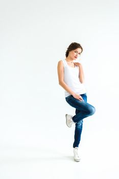 cheerful girl in a white t-shirt and dark blue jeans in the studio on a white background stands, sits, runs