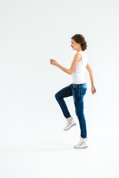 cheerful girl in a white t-shirt and dark blue jeans in the studio on a white background stands, sits, runs