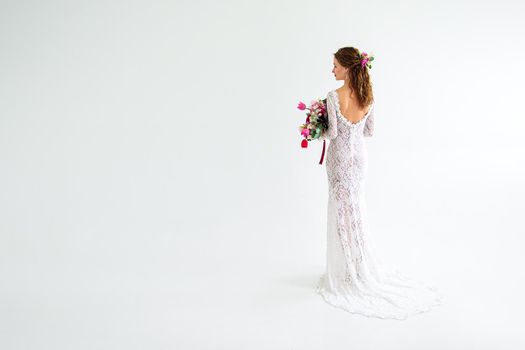 joyful girl bride in a white knitted dress posing with a bouquet of flowers in the studio on a white background