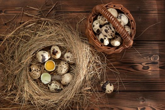 Several quail eggs in a decorative nest of straw and in a basket on a wooden table, flatlay.