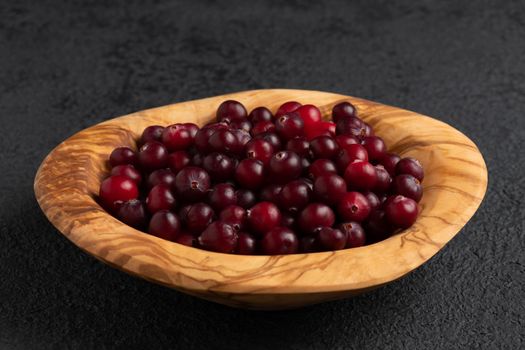 Ripe fresh cranberries in a wooden bowl on a black table.