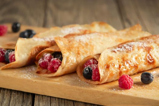 Pancakes stuffed with fresh berries on a wooden board close-up.