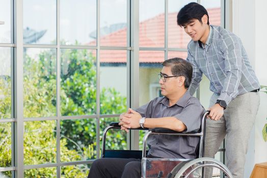 Asian senior disabled businessman in wheelchair discuss interacting together with the team in the office. The old man in a wheelchair and his young son talking to and comforting bound father