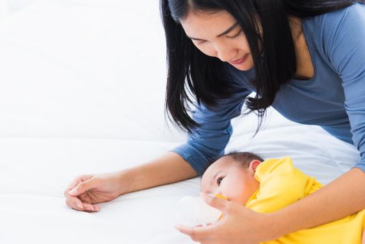 Portrait of beautiful young Asian mother holding and feeding infant newborn baby from milk bottle in a white bed, The child drinking milk from mom, Healthcare and medical