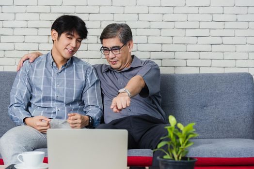 Asian senior businessman with laptop computer discuss together with young team in office. Father man and his son sit on sofa talking chatting on video call conference on laptop in living room at home