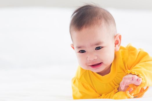 Portrait of beautiful young Asian newborn little baby prone on the bed at home, Happy baby smile wears a yellow shirt relaxing in the room, Family morning at home