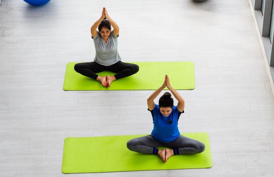 Two Asian women sporty attractive people practicing yoga lesson together, working out at the fitness GYM, Young and senior female exercising do yoga in yoga classes, sport healthy lifestyle
