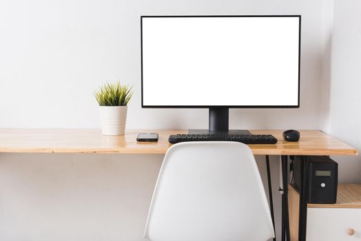 Computer monitor with white blank screen on the business desk with wireless mouse, keyboard at home office over white wall background, Photo of equipment contemporary workspace