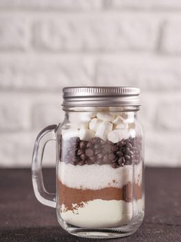 Hot chocolate mix in mason jar. Homemade mix from cocoa, dry milk, sugar, chocolate chips and marshmallows. Christmas and winter holiday budget-friendly holiday gifts idea. Copy space