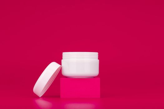 Opened jar of cream on pink podium against pink background with copy space. Jar for cosmetic product. Concept of skin care and beauty or anti aging skin treatment