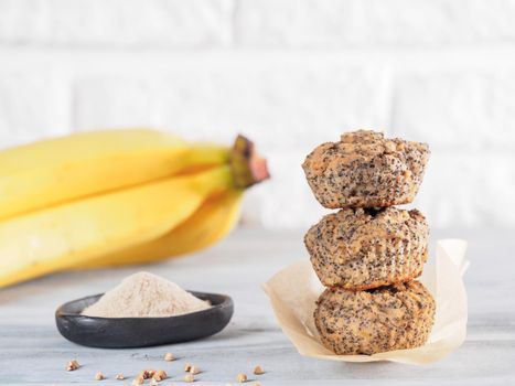 Healthy gluten-free homemmade banana muffins with buckwheat flour. Stack of three vegan muffins with poppy seeds on gray wooden table. Copy space