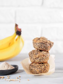 Healthy gluten-free homemmade banana muffins with buckwheat flour. Stack of three vegan muffins with poppy seeds on gray wooden table. Copy space