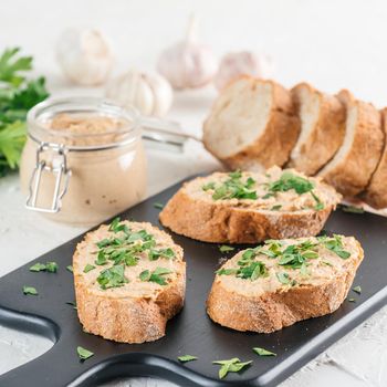 Close up view of slice bread with homemade turkey pate and fresh green parsley on black kutting board over white concrete background, Shallow DOF. Selective focus