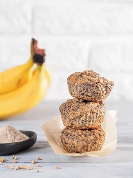 Healthy gluten-free homemmade banana muffins with buckwheat flour. Stack of three vegan muffins with poppy seeds on gray wooden table. Copy space