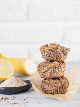 Healthy gluten-free homemmade banana muffins with buckwheat flour. Stack of three vegan muffins with poppy seeds and lemon on gray wooden table. Copy space