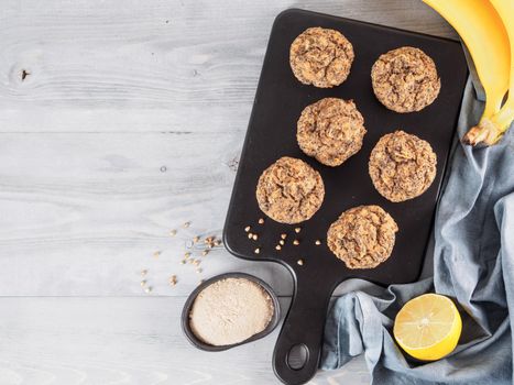 Healthy gluten-free homemmade banana muffins with buckwheat flour. Vegan muffins with poppy seeds on black cutting board over gray wooden table. Copy space. Top view or flat lay.