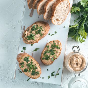 Top view of slice bread with homemade turkey pate and fresh green parsley on white rustic kutting board over white concrete background, Shallow DOF. Selective focus