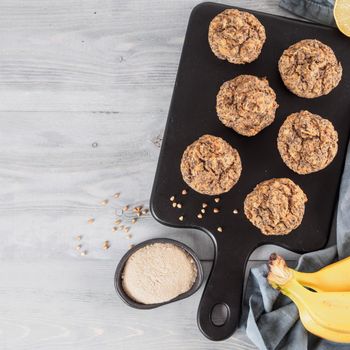 Healthy gluten-free homemmade banana muffins with buckwheat flour. Vegan muffins with poppy seeds on black cutting board over gray wooden table. Copy space. Top view or flat lay.