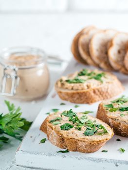 Close up view of slice bread with homemade turkey pate and fresh green parsley on white rustic kutting board over white concrete background, Shallow DOF. Selective focus