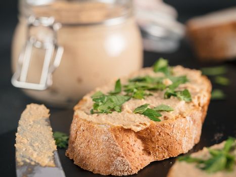 Extreme close up view of slice bread with homemade turkey pate and fresh green parsley on black kutting board over black cement background, Shallow DOF. Selective focus