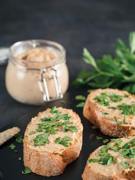 Close up view of slice bread with homemade turkey pate and fresh green parsley on black kutting board over black cement background, Copy space.